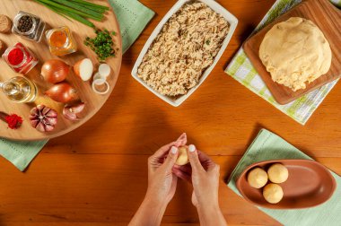 Kadın elleri ahşap mutfak masasında Brezilya kroketi (coxinha de frango) hazırlıyor.