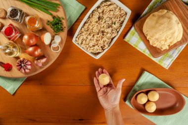 Kadın elleri ahşap mutfak masasında Brezilya kroketi (coxinha de frango) hazırlıyor.