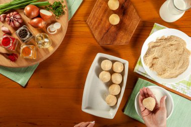 Kadın elleri Brezilya kroketini (coxinha de frango) ahşap mutfak masasında ekmek kırıntılarıyla hazırlıyor.