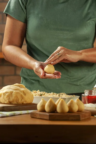 Kadın elleri tahtadan bir masada Brezilya kroketi (coxinha de frango) hazırlıyor..