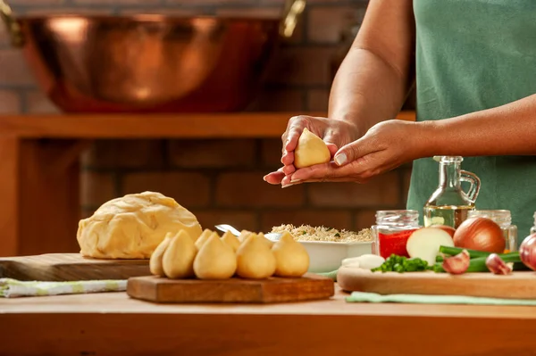 Kadın elleri tahtadan bir masada Brezilya kroketi (coxinha de frango) hazırlıyor..