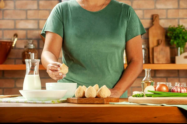 Kadın elleri ahşap bir masada Brezilya kroketi (coxinha de frango) pişiriyor..