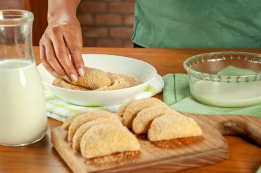 Tahta bir masada Brezilya usulü ekmek doldurulmuş kroket (risolis de carne) yiyen kadın. Üst görünüm.
