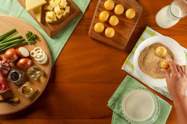 Tahta bir masada Brezilya peyniri doldurulmuş kroket (bolinha de queijo) yiyen bir kadın. Üst görünüm.