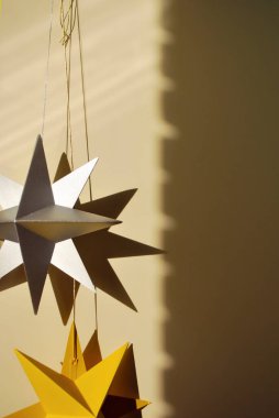 Noel süslemeleri karton ya da kağıt oyuncaklar gri ve sarı renkli yıldızların arka planında estetik güneş ışığı gölgeleri var. Sıfır atık. Sürdürülebilir eko yaşam tarzı. Çevre dostu yeniden kullanılabilir materyallerden DIY ev dekoru
