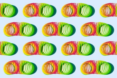 Soluk mavi arka planda gölgeleri olan esnek gökkuşağı çocukların retro oyuncaklarından bir desen. Sinsi. Stres önleyici oyuncak. Paket kağıtları, kumaşlar, kartlar için tasarım. Esneklik sembolü. Duvar kağıdı için klorlu desen