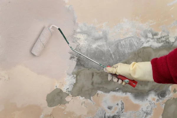塗料ローラーを使用して家の中で古い壁をペイント手袋で労働者の手の閉鎖 — ストック写真