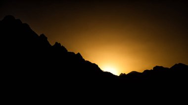Ağaçların siluetleri dağların arka planına ve turuncu gökyüzüne karşı. Valbona Valley Ulusal Parkı. Prokletije Dağları. Arnavut Alpleri.