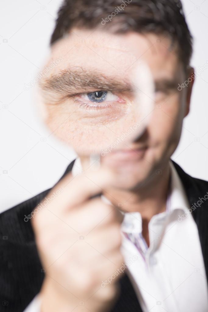 Serious looking man watching with magnifying glass