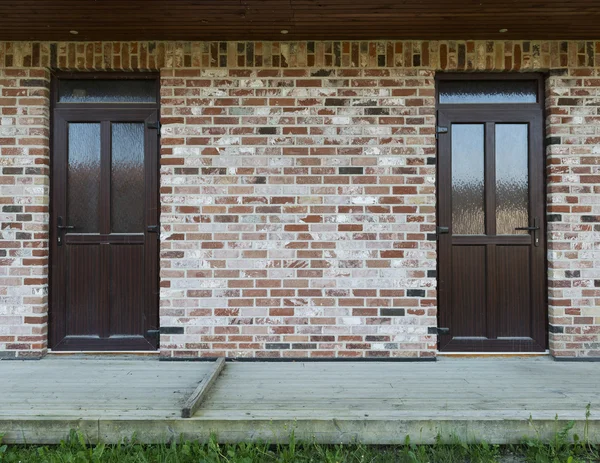 Brick wall with two doors, wooden terrace and grass