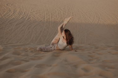 Kumsalda poz veren bej elbiseli güzel bir esmer. Çekici kadın mutlu bir şekilde dans ediyor, çölde poz veriyor.