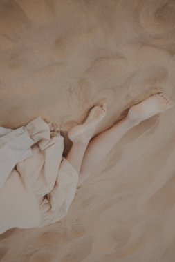 Kumsalda bej elbiseli güzel bir esmer kadın yatıyor.