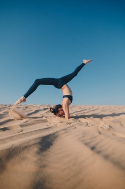 Kumsalda poz veren siyah elbiseli güzel bir esmer. Çekici kadın mutlu bir şekilde dans ediyor, mavi gökyüzüne karşı poz veriyor.
