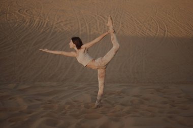 Kumsalda poz veren bej elbiseli güzel bir esmer. Çekici kadın mutlu bir şekilde dans ediyor, çölde poz veriyor.