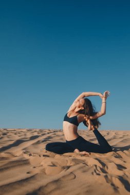 Kumsalda poz veren siyah elbiseli güzel bir esmer. Çekici kadın mutlu bir şekilde dans ediyor, mavi gökyüzüne karşı poz veriyor.