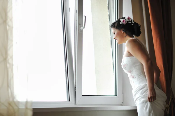 Jeune belle mariée regardant par la fenêtre tout en souriant — Photo