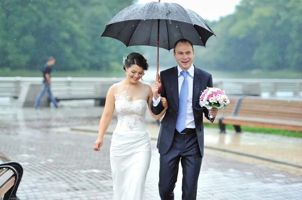 Молодой счастливый жених и невеста идут под дождем — стоковое фото