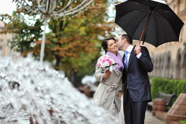 Young happy bride and groom kissing by the rain — Stock Photo, Image