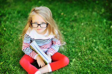 küçük kız portre gözlük takan bir parkta bir kitapla