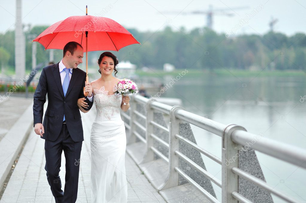 Wedding couple waking by the rain under umbrella