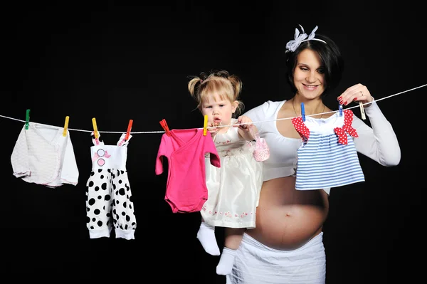 Grávida jovem mãe com seu bebê menina pendurado roupas — Fotografia de Stock