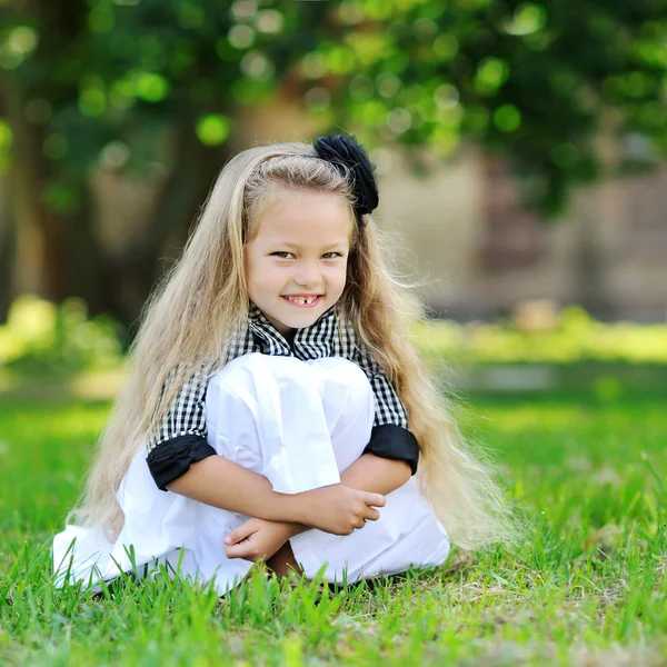 Doce menina sentada em uma grama e sorrindo — Fotografia de Stock