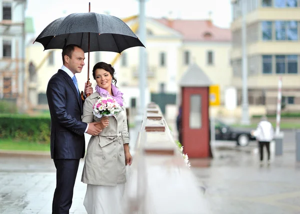 Brud och brudgum gömmer sig från regn i en gammal stad — Stockfoto