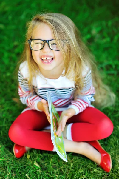 Adorable little girl in glasses holding book and laughing - outd — Stock Photo, Image