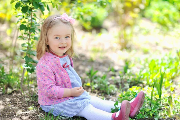 Niedliches kleines Mädchen, das in einem Garten sitzt und dich ansieht - hell — Stockfoto