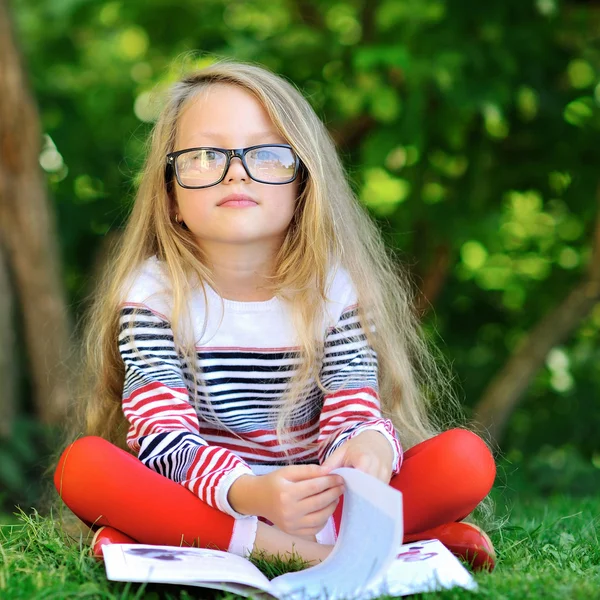 Portret van lief klein meisje dragen bril, leesboek, sit — Stockfoto