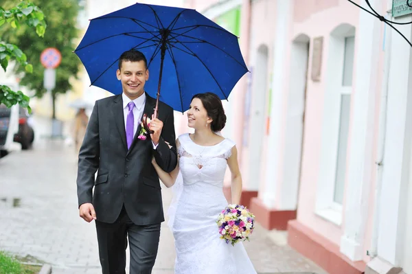 Молодая счастливая супружеская пара, идущая под дождем в старом городе — стоковое фото