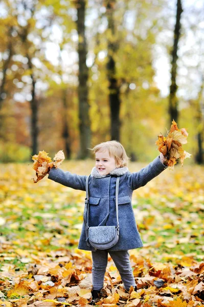 Kleines Mädchen wirft Blätter in Herbstpark — Stockfoto