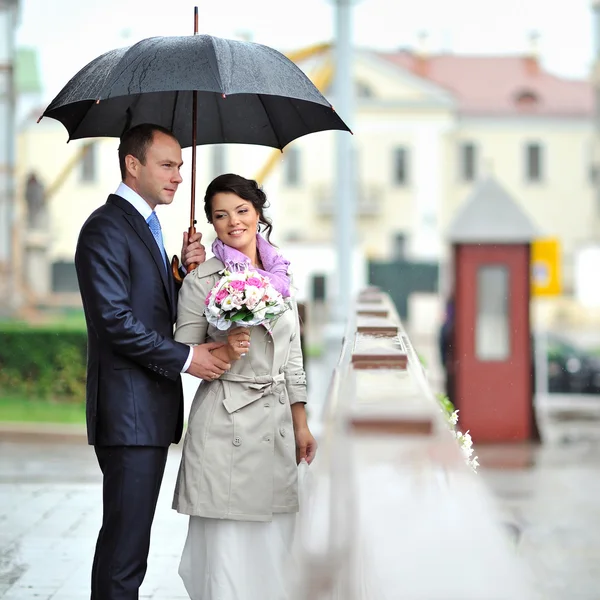 Gelin ve damat eski bir kasabada yağmurdan saklanıyor. — Stok fotoğraf