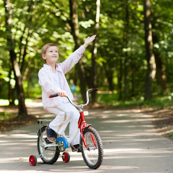 Outdoor Portret van schattige jongen op een fiets glimlachend en wijst een — Stockfoto