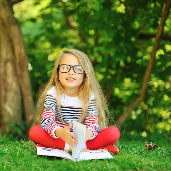 Menina bonito com um livro em um parque de verão verde — Fotografia de Stock