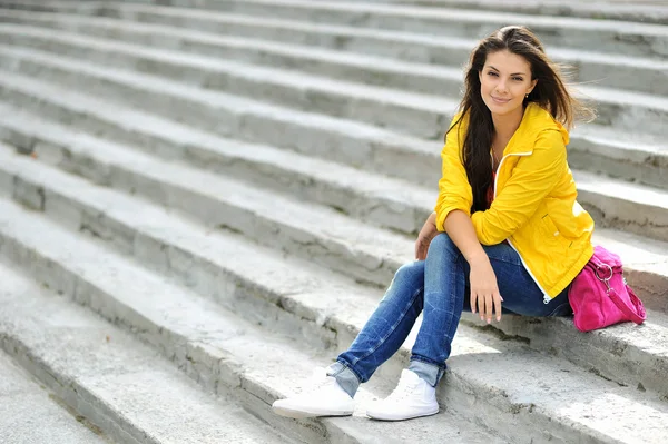 Stylish beautiful teen girl sitting on a stairs in colorful clot — Stock Photo, Image