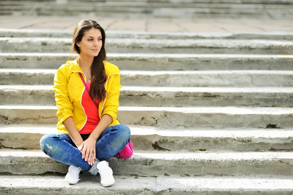 Elegante bella ragazza seduta su una scala in vestiti colorati — Foto Stock