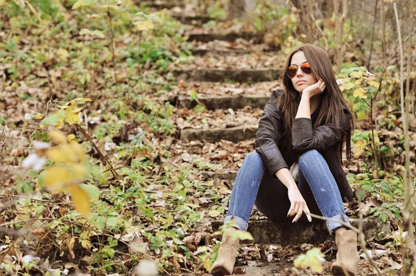 Menina da moda sentado em um parque usando óculos de sol — Fotografia de Stock