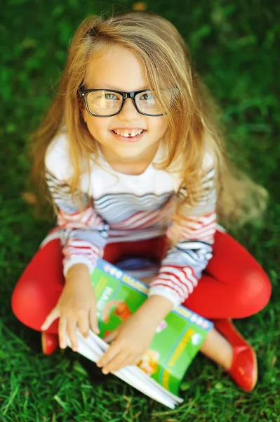 Attractive little girl with book in a park — Stock Photo, Image