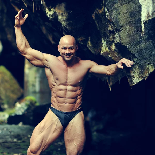 Retrato de um fisiculturista muscular bonito posando em uma caverna — Fotografia de Stock