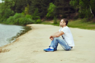 Lonely young man sitting near a lake in a forest clipart