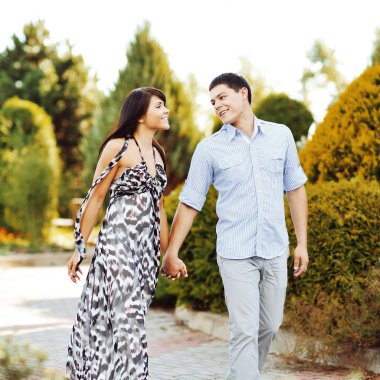 Yeşil bir parkta birlikte yürüyen mutlu genç çift. 