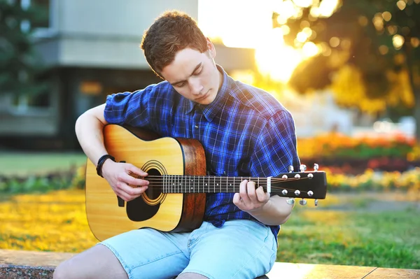Mladý muž, hraje na akustickou kytaru v parku — Stock fotografie