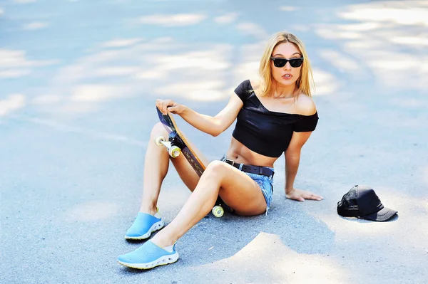 Jeune femme assise sur un skateboard - en plein air — Photo