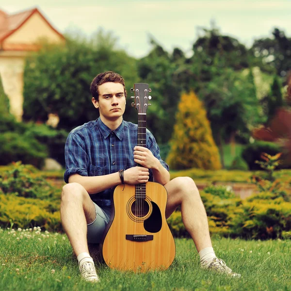 Young stylish hipster man with guitar in the park — Stock Photo, Image