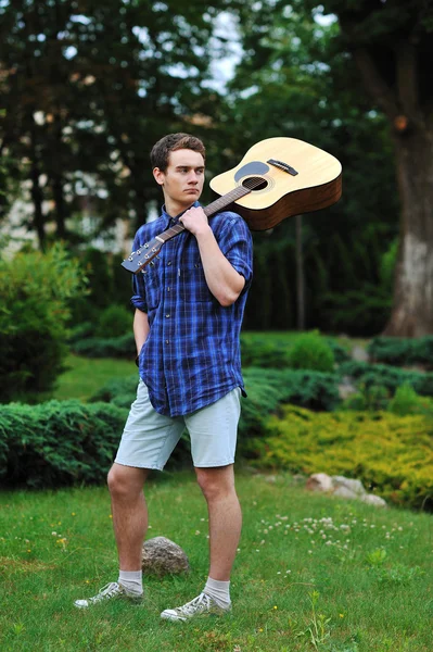 Mladý muž s akustickou kytaru v parku — Stock fotografie