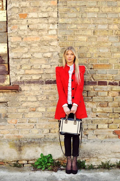 Chica de moda en vestido rojo con bolsa de pie cerca de una pared — Foto de Stock