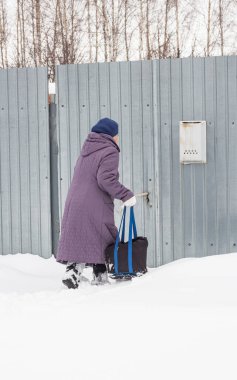 Yaşlı bir kadın kar yığınlarında zar zor çanta taşıyabilir..