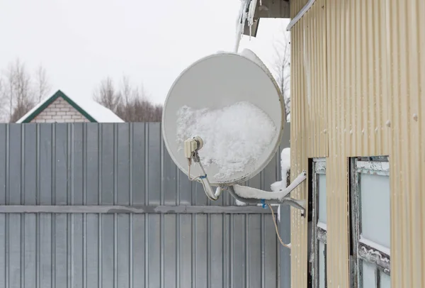 降雪後の雪の中の家の壁に固定された衛星料理 ロイヤリティフリーのストック写真