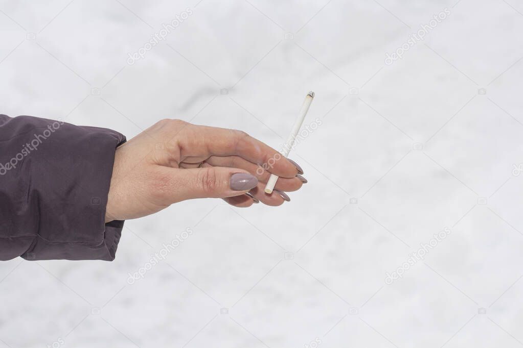 a smoldering cigarette in women's hands against the background of snow with a copy of space.